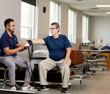 A male physical therapist doing hand mobility exercises with an elderly male patient.